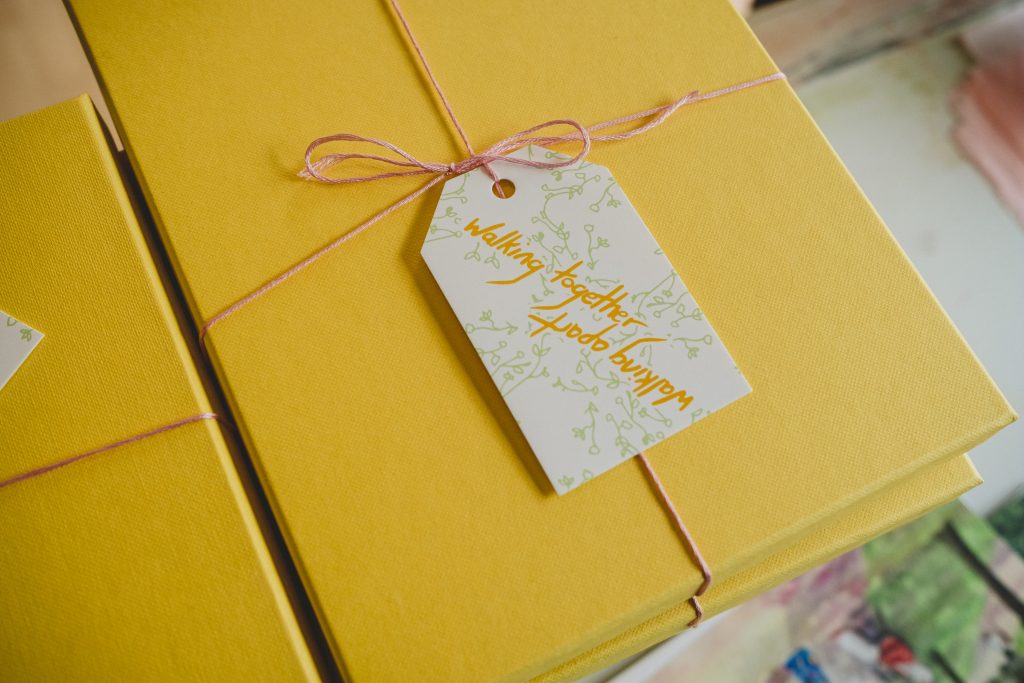 A stack of yellow gift boxes, tied with pink thread and a gift tag that reads 'Walking together, walking apart'