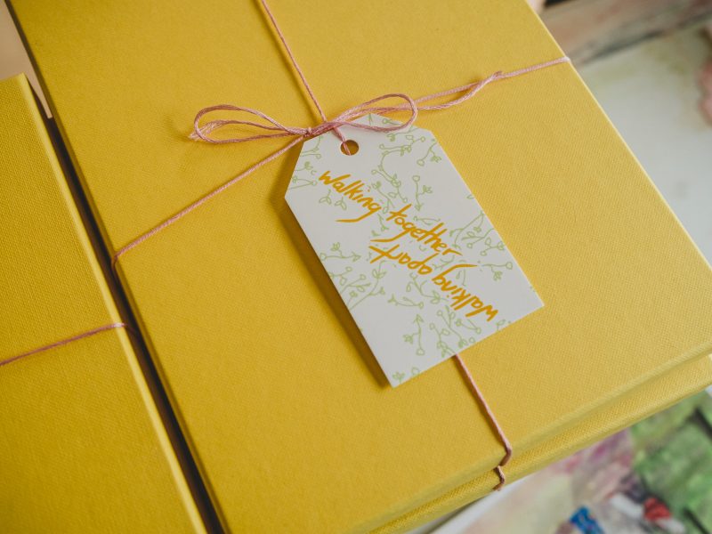 A stack of yellow gift boxes, tied with pink thread and a gift tag that reads 'Walking together, walking apart'