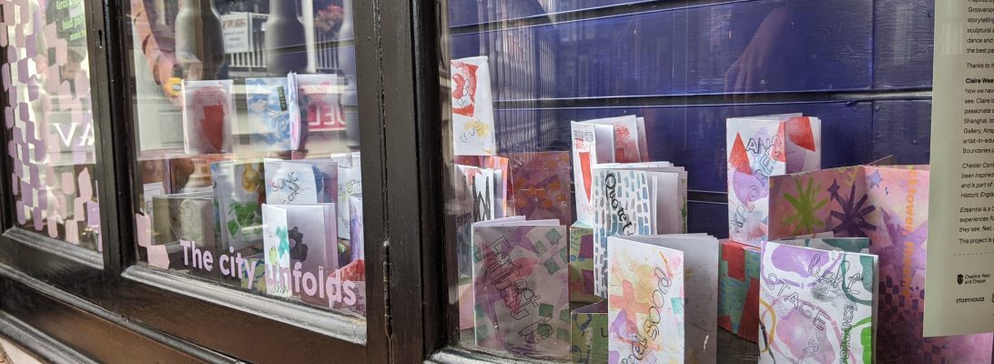 The base of a glass cabinet has small books made from paper that are printed with colourful architectural shapes and feature words including "quote, stage, performance, feel good"