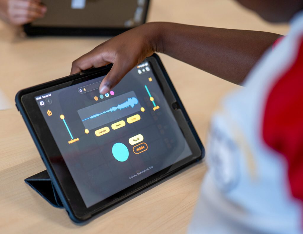 A child touches an ipad screen that shows a visual of a sound wave and various buttons
