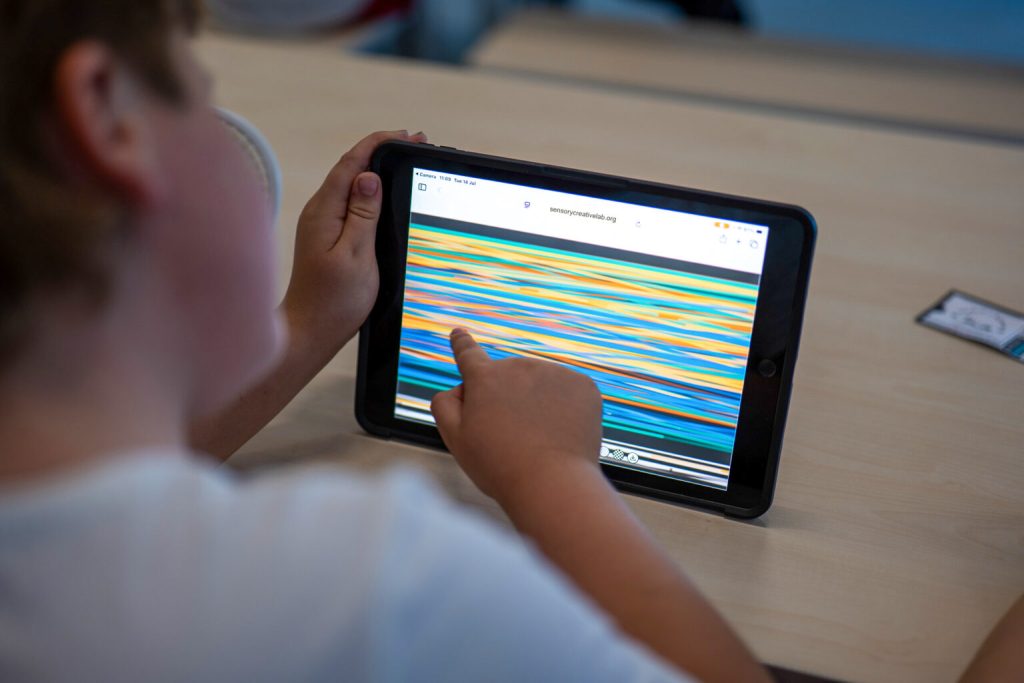 A child touches an ipad screen that is streaked with colourful stripes