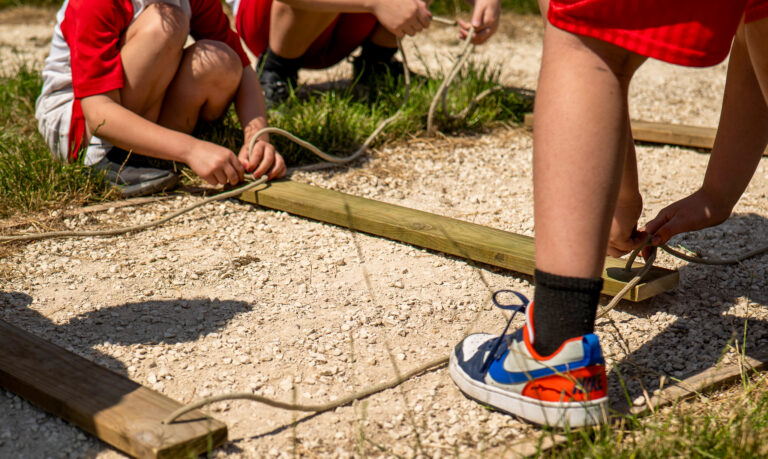 children are kneeling on the floor joining planks of wood with rope to form a railway track