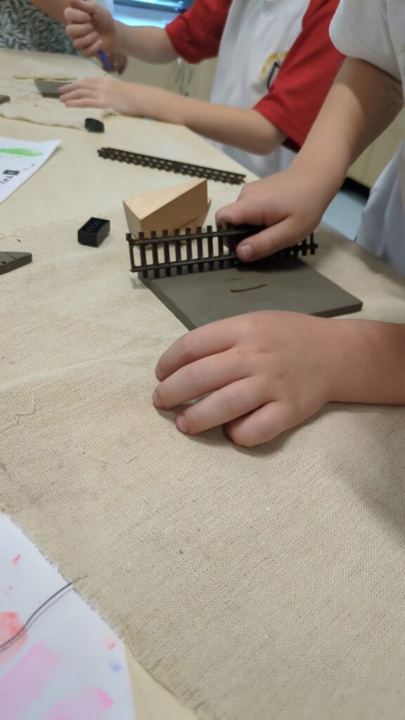 A child presses a piece of model railway track into a slab of clay